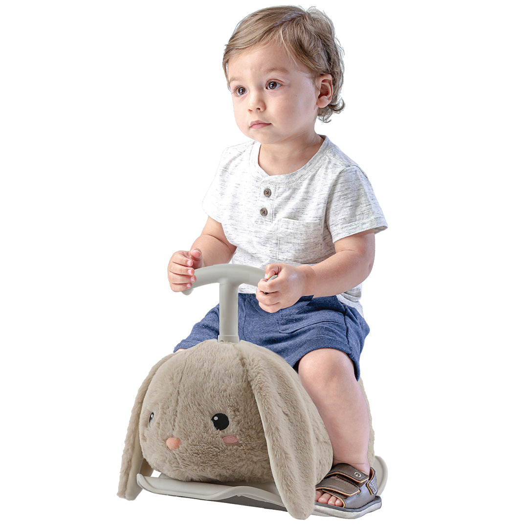 Een peuterjongen zit op de Yvolution beige pluche konijn loopwagen en hobbeldier.