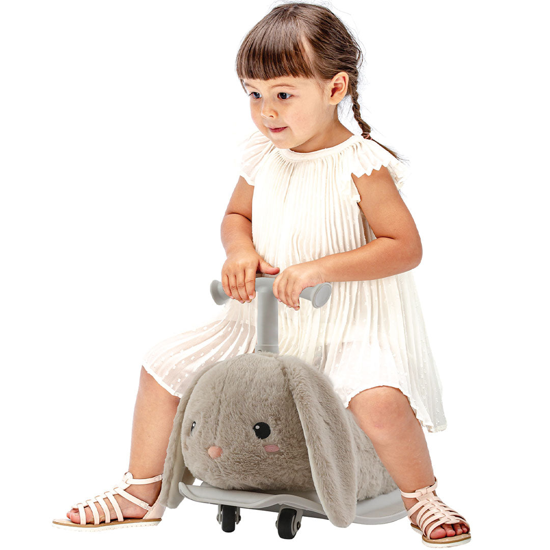 Een peutermeisje zit op de Yvolution beige pluche konijn loopwagen en hobbeldier.