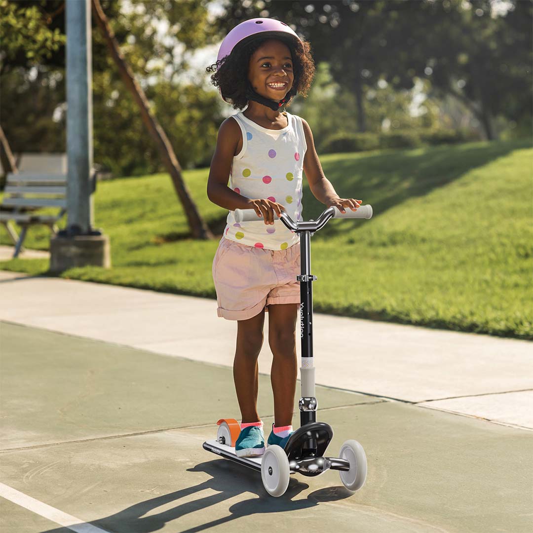Een lachend kind met helm rijdt op de Yvolution kinderstep classic glider buiten op een pad.