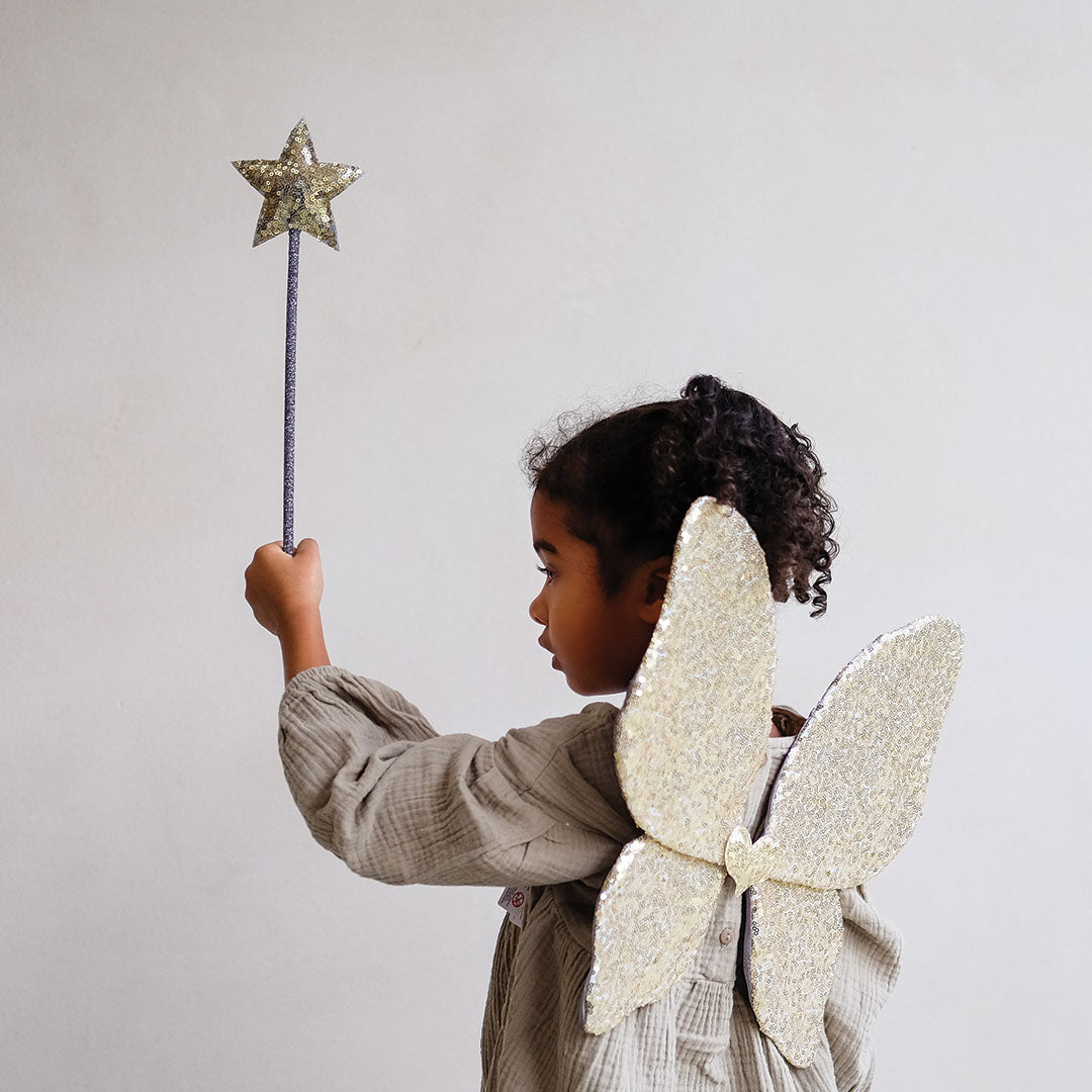 Meisje met gouden pailletten vlindervleugels houdt een mimi & lula toverstaf met gouden ster omhoog.
