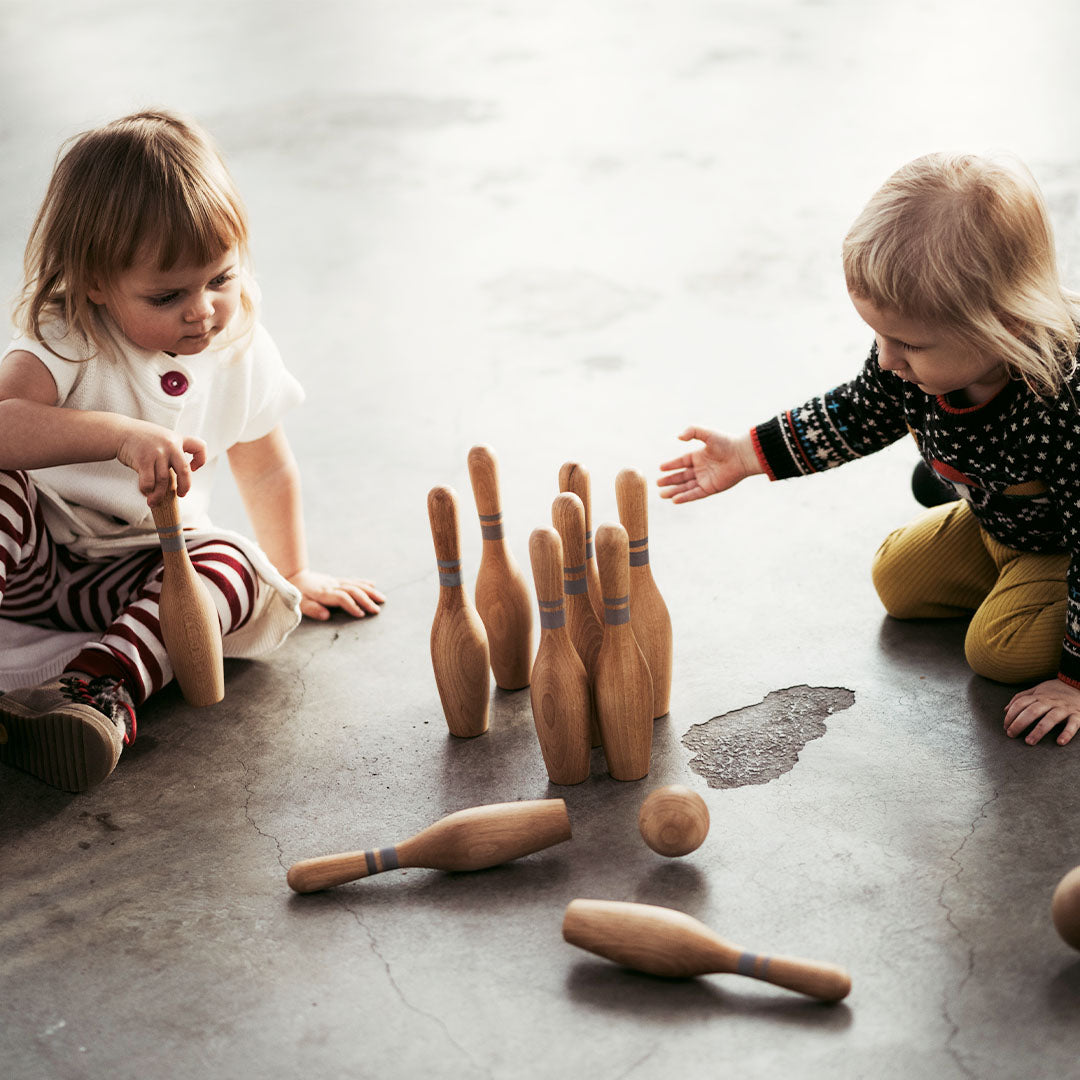Twee jonge kinderen spelen met het Wooden Story houten bowlingspel op een grijze vloer.
