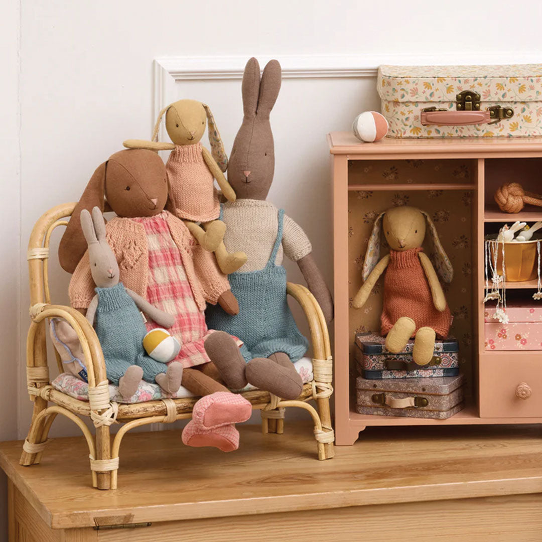 Een groep Maileg knuffelkonijnen zit op een rieten bankje en naast een houten kastje in een kinderkamer setting.