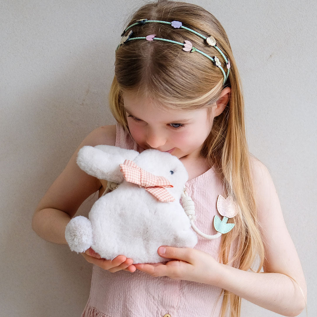 Een meisje houdt het mimi & lula fluffy konijnen schoudertasje tegen haar wang, met een bloemenhoofdband op.