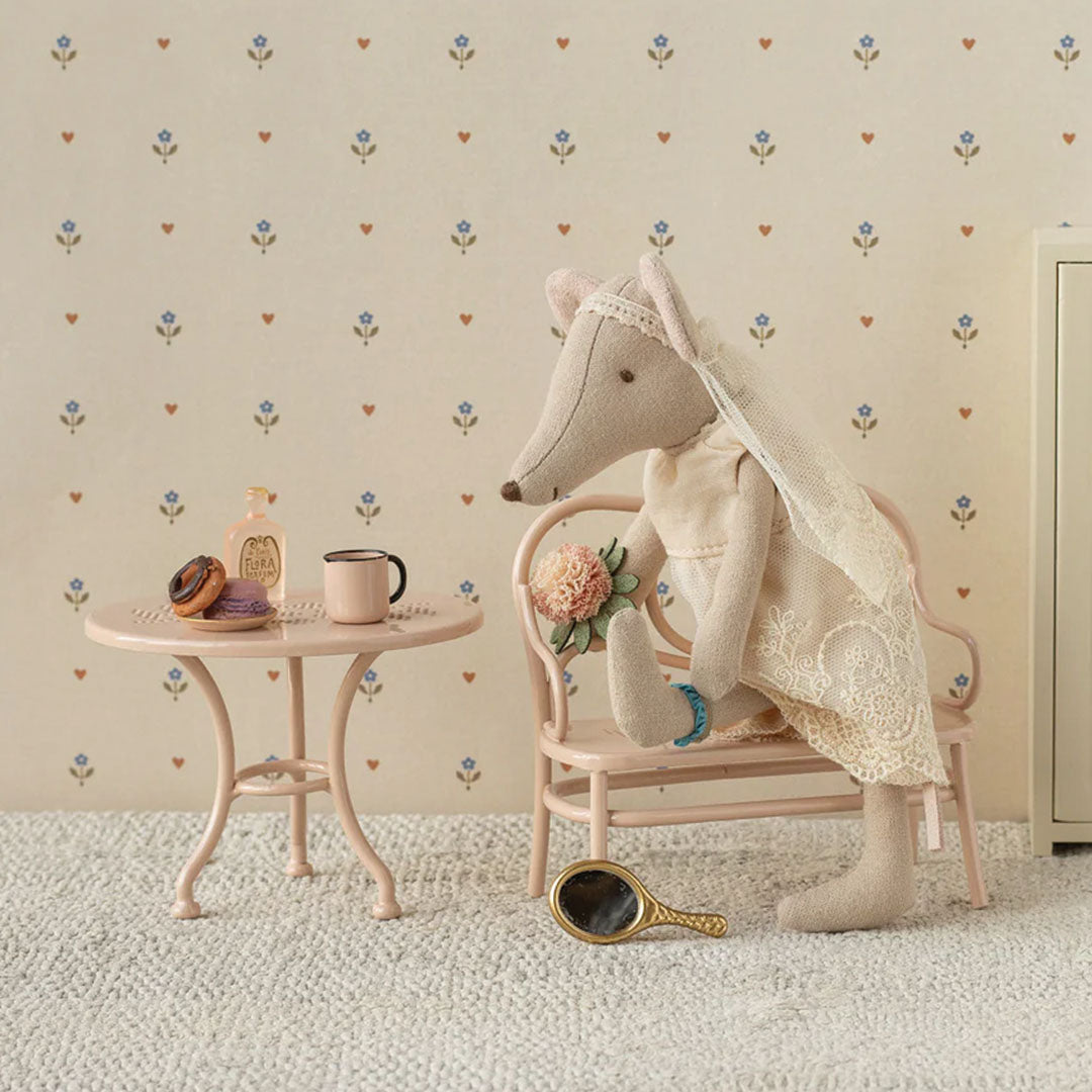 Maileg muispop in beige trouwjurk met sluier en bloemenboeket, zittend op een roze stoel.
