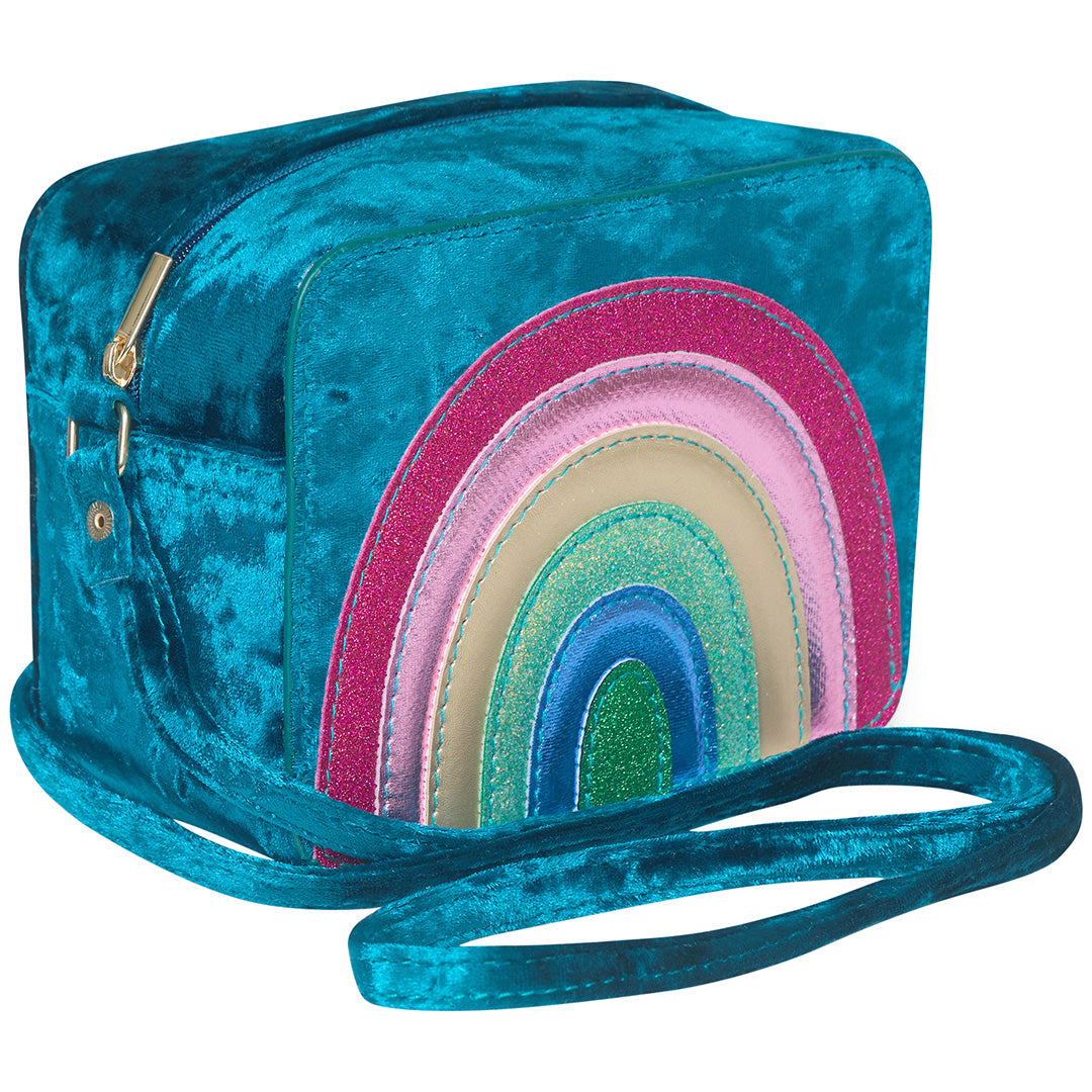 mimi & lula blauw fluwelen schoudertasje voor kinderen met een kleurrijke regenboog op de voorkant, schuin gefotografeerd.