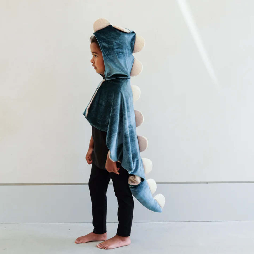 Kind draagt de Mimi & Lula groene fluwelen dinosaurus verkleedcape met lichtgekleurde stekels, van de zijkant gefotografeerd.
