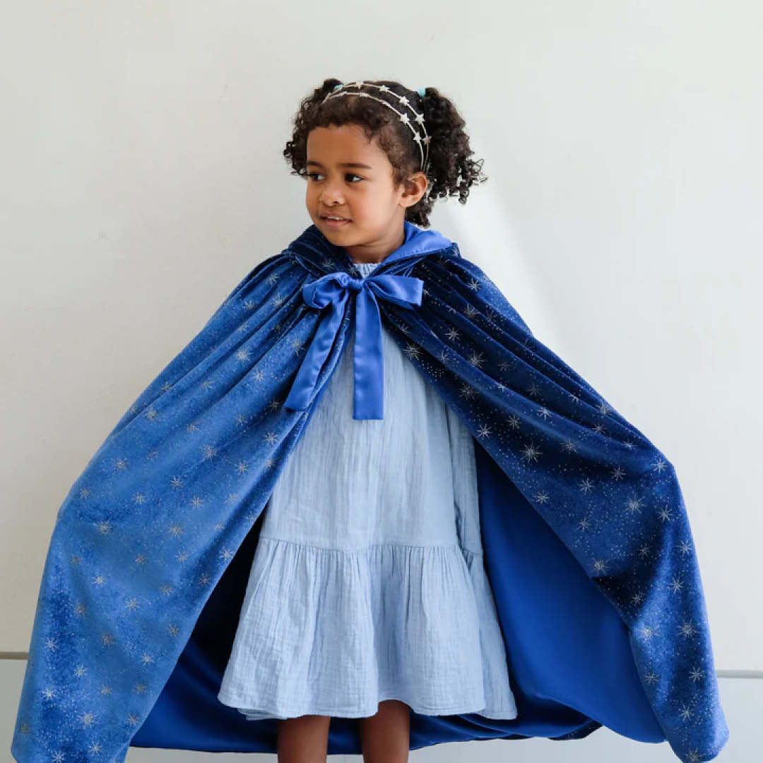Meisje van voren gezien dat de mimi & lula blauwe fluwelen verkleedcape met sterren draagt, open over een lichtblauwe jurk.