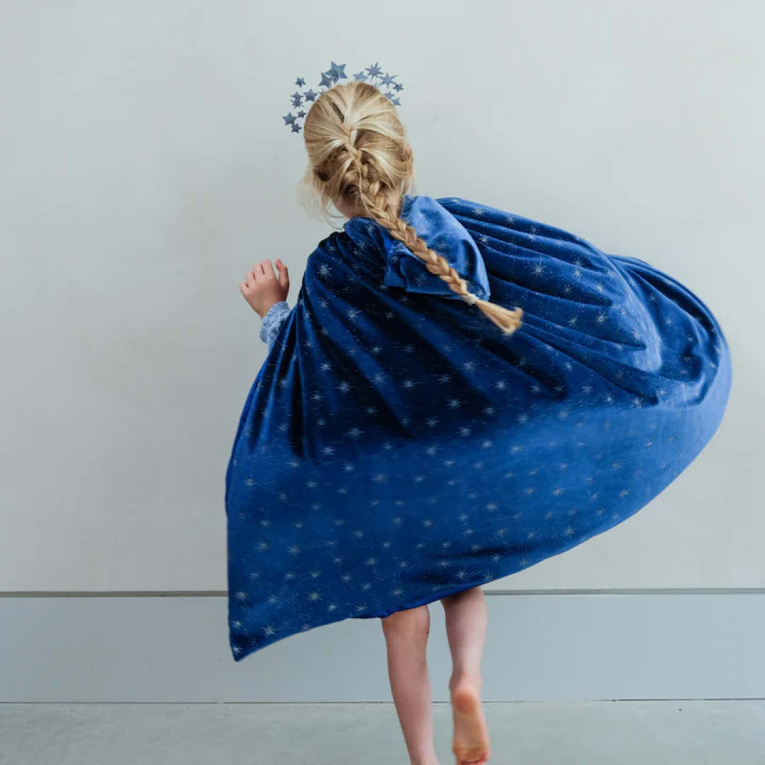 Meisje van achteren gezien dat de mimi & lula blauwe fluwelen verkleedcape met sterren draagt en ronddraait.