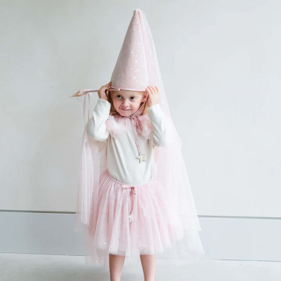 Een meisje draagt de roze mimi & lula verkleedcape met glittersterren en een bijpassende hoed, en lacht naar de camera.