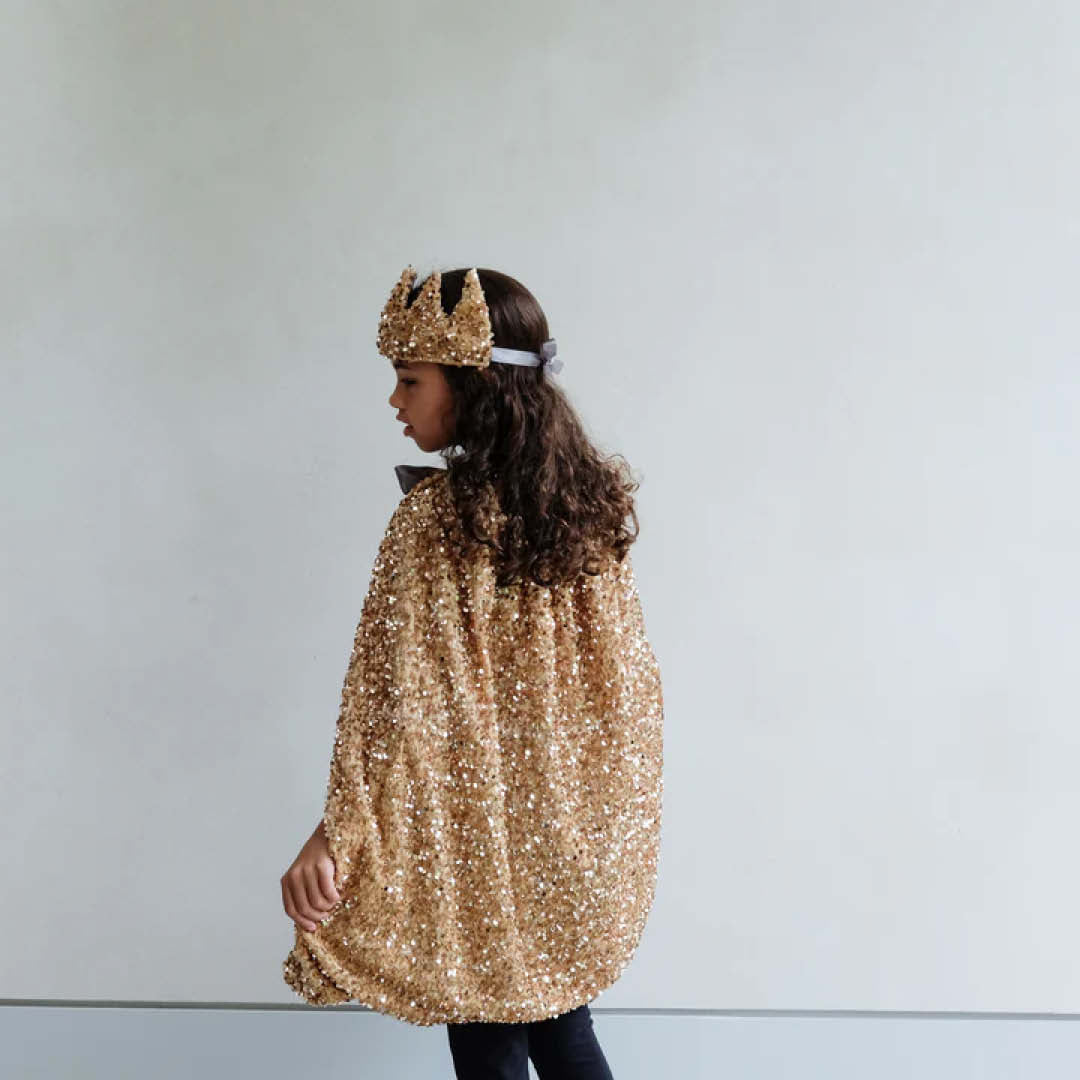 Kind draagt de gouden pailletten verkleedcape van Mimi & Lula en een bijpassende kroon, van opzij gezien.