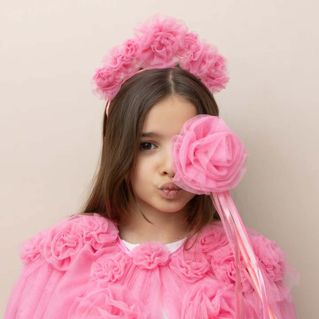 Meisje met roze verkleedkleding en een roze toverstaf met bloem voor haar gezicht.