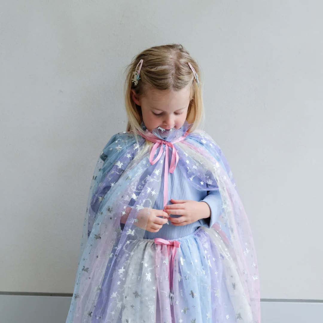 Een kind draagt de mimi & lula verkleedrok en een bijpassende cape met regenboog ombre en sterren.