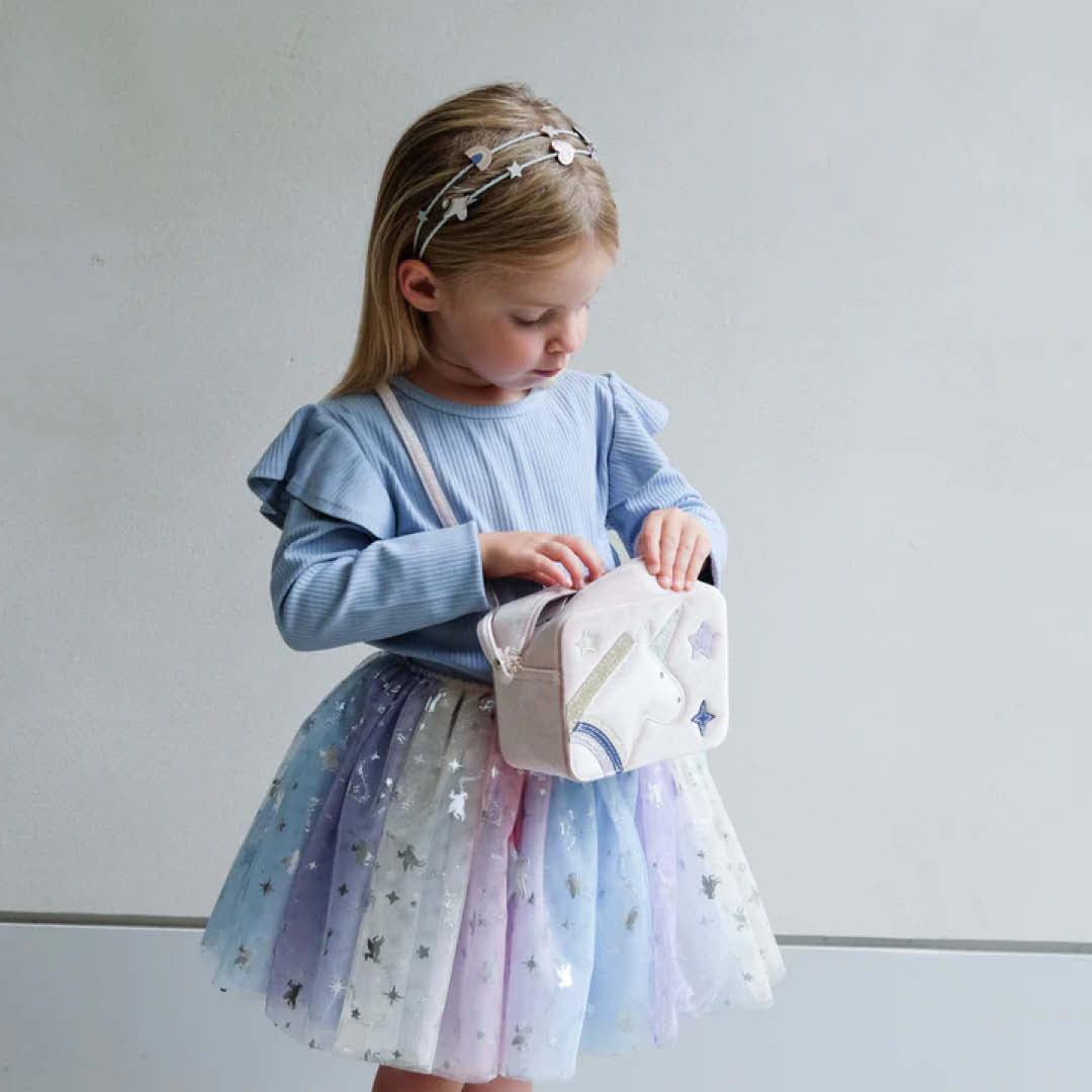 Een kind draagt de mimi & lula verkleedrok met regenboog ombre en sterren, en kijkt in een tasje.