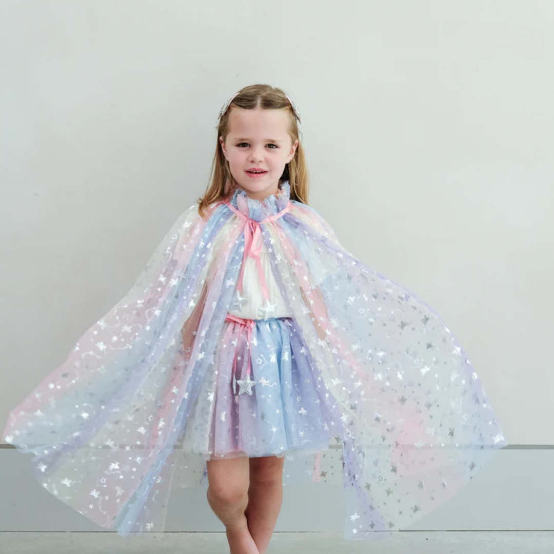 Een kind draagt de mimi & lula verkleedrok en cape met regenboog ombre en sterren, en spreidt de cape uit.