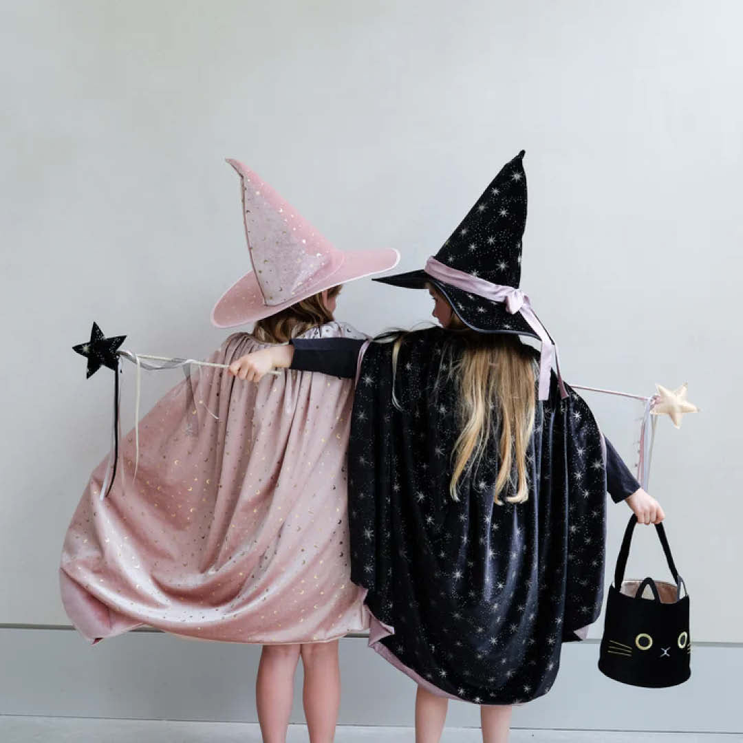 De achterkant van twee meisjes in roze en zwart heksenkostuum met sterren, met capes en toverhoeden.