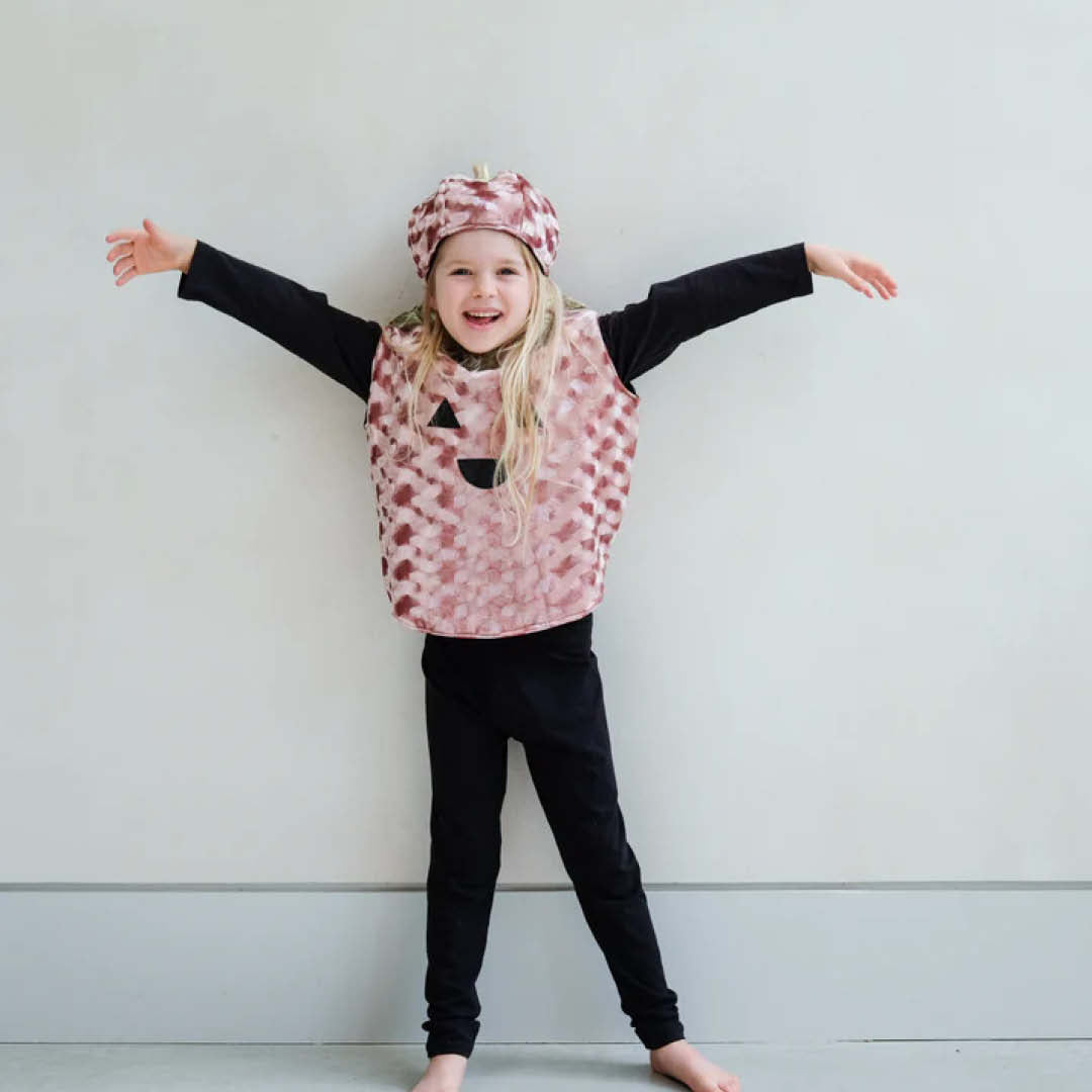 Een lachend kind draagt de roze pompoen tuniek en muts met uitgestrekte armen.