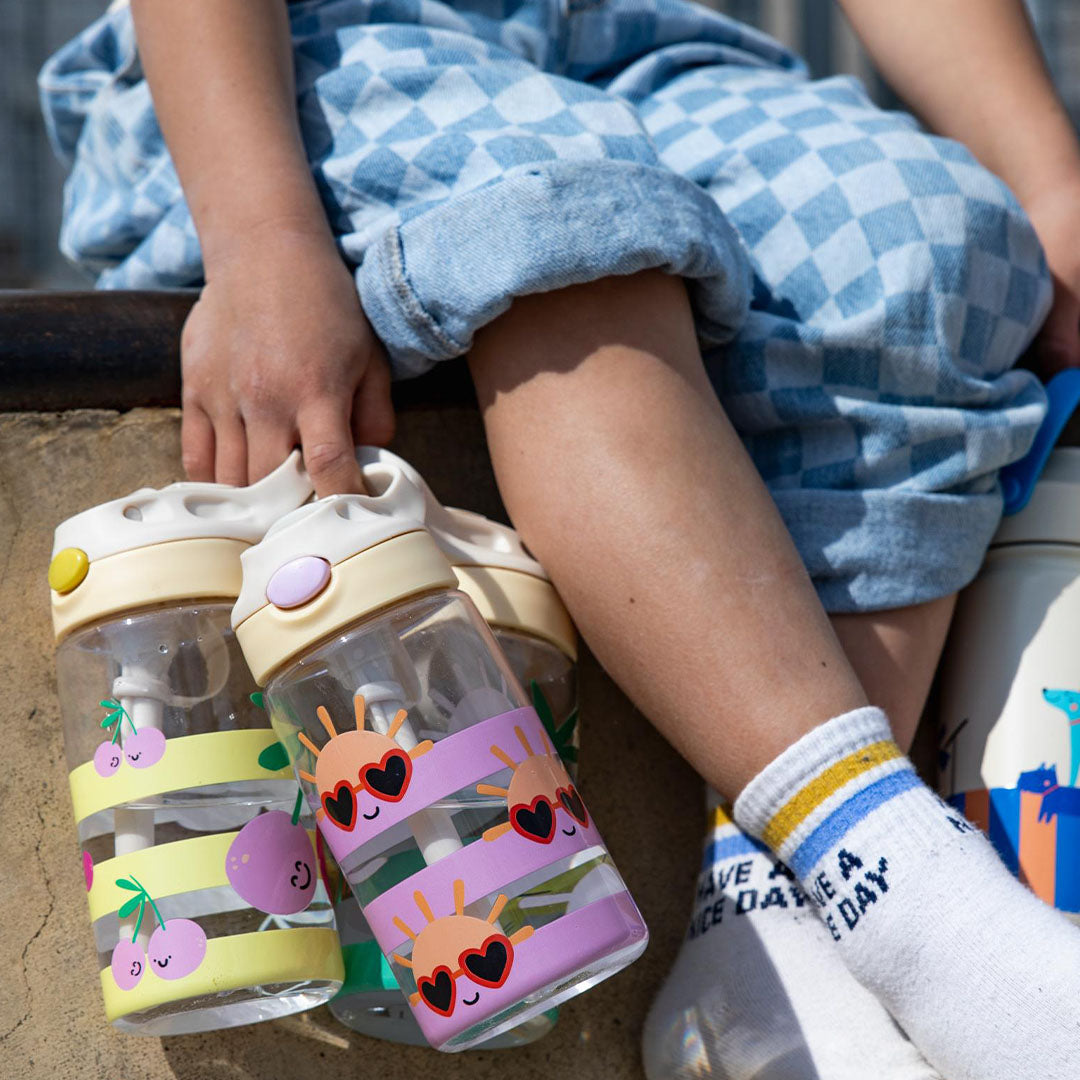 Drie the cotton cloud kinderdrinkflessen met verschillende patronen naast de benen van een kind.