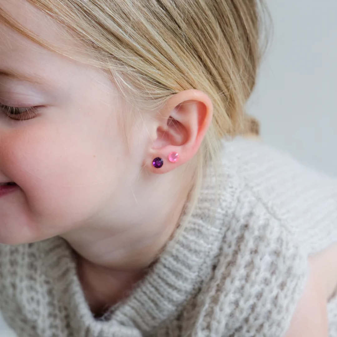 Close-up van een kinder oor met twee roze plakoorbellen.