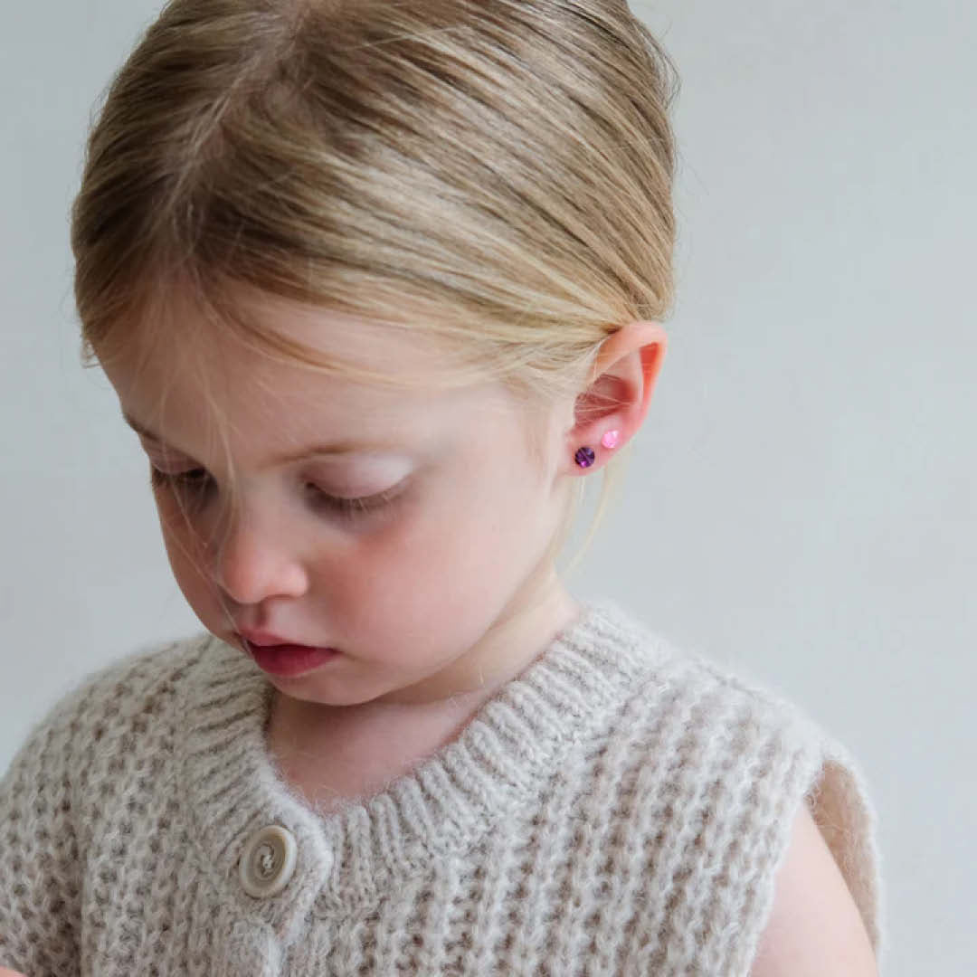 Een kind met blonde haren draagt twee roze plakoorbellen aan één oor.