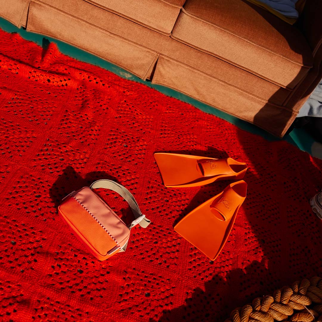 Colourblocked heuptas op een rood kleed met oranje zwemvliezen ernaast.