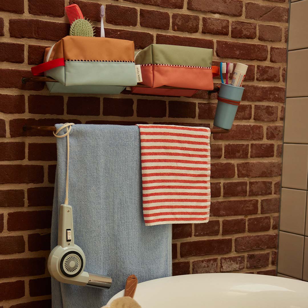 Twee Sticky Lemon colourblocking toilettassen hangen aan een houten rek in een badkamer.
