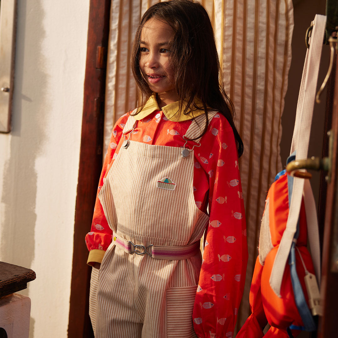 Kind draagt de Sticky Lemon gestreepte kinderriem over een beige gestreepte overall.