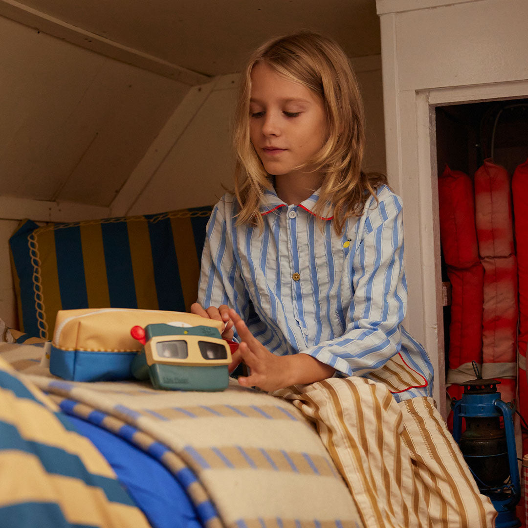 Een kind in gestreepte pyjama kijkt door de Sticky Lemon viewmaster op bed.