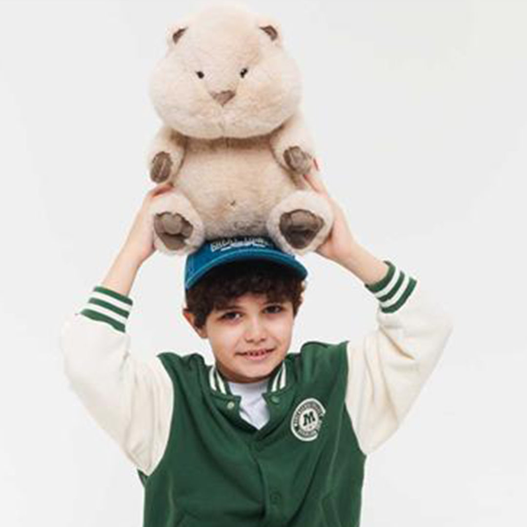 Een jongen met een pet balanceert de pluchen hamster knuffel op zijn hoofd.