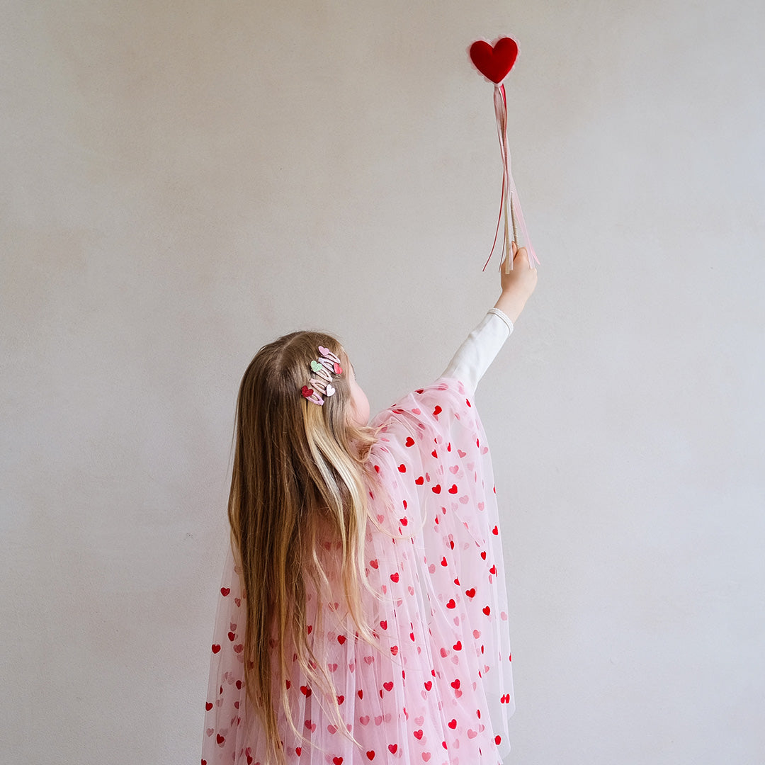 Meisje met blond haar houdt de toverstaf met rood hart omhoog, gezien van achteren.
