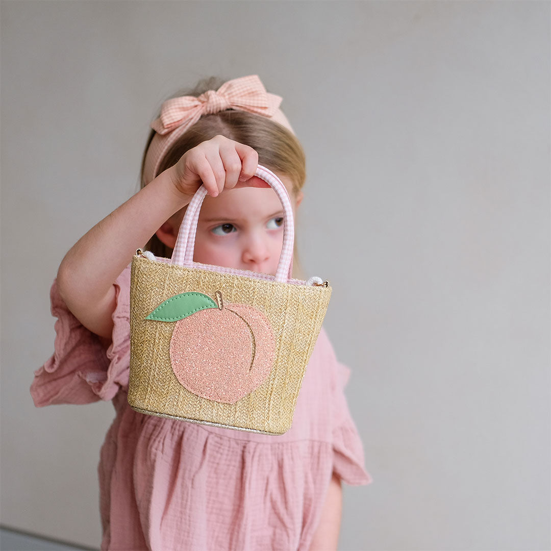 Een kind met een roze jurk houdt de mimi & lula kinder emmertas met perzikapplicatie vast.