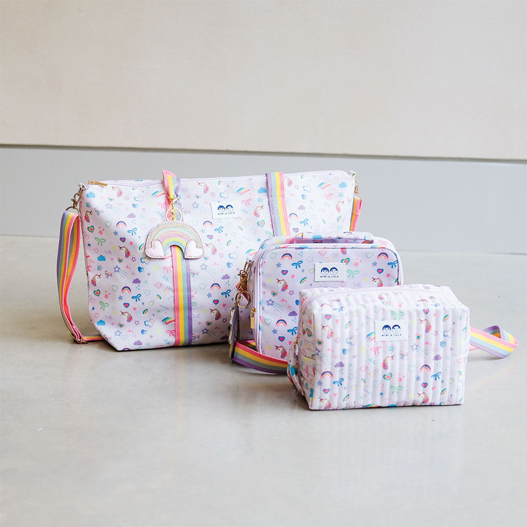 Een collectie van Mimi & Lula tassen met eenhoorn- en regenboogpatroon, inclusief een weekendtas, lunchbox en toilettas.