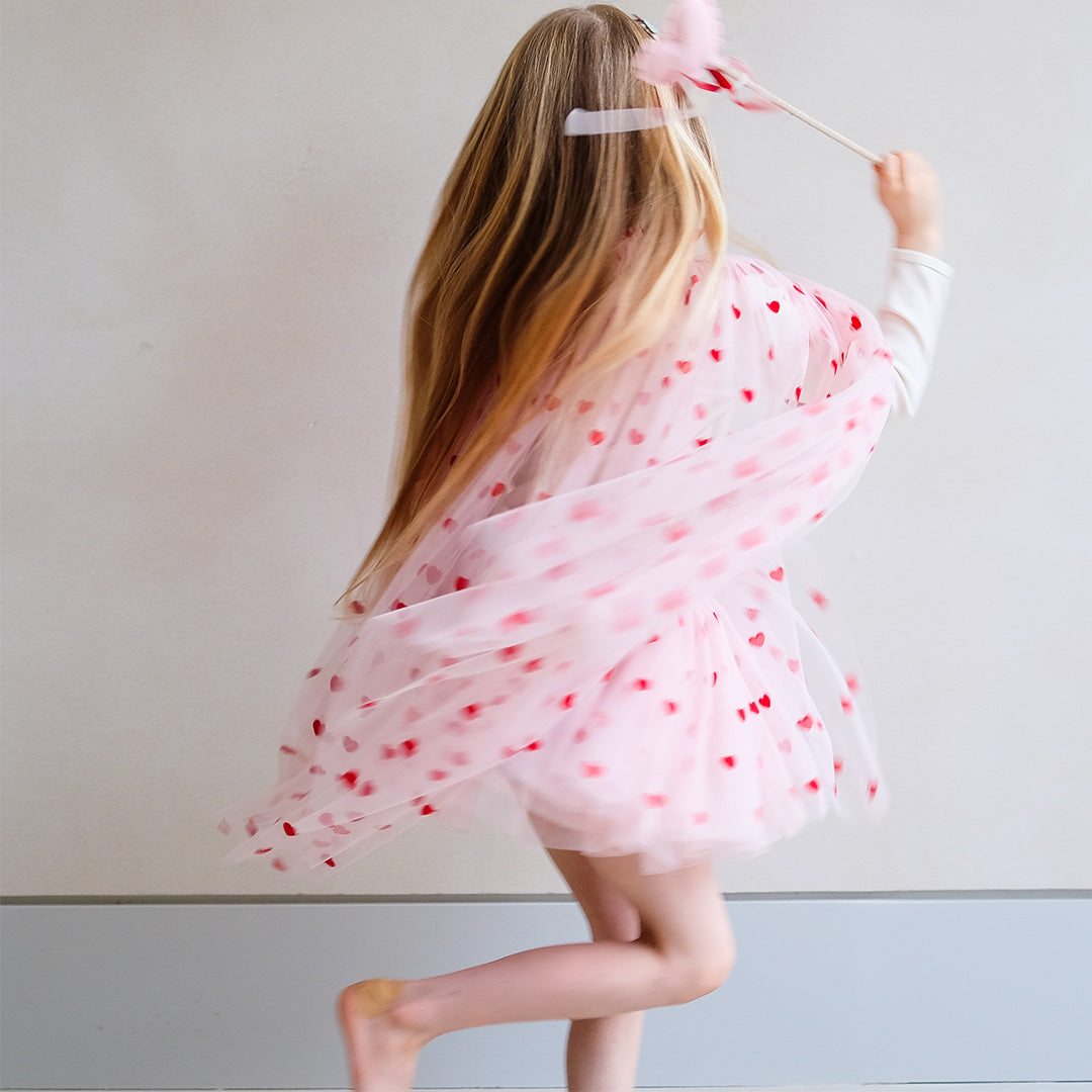 Een meisje rent met de roze kinder verkleedcape met harten, van achteren gefotografeerd.