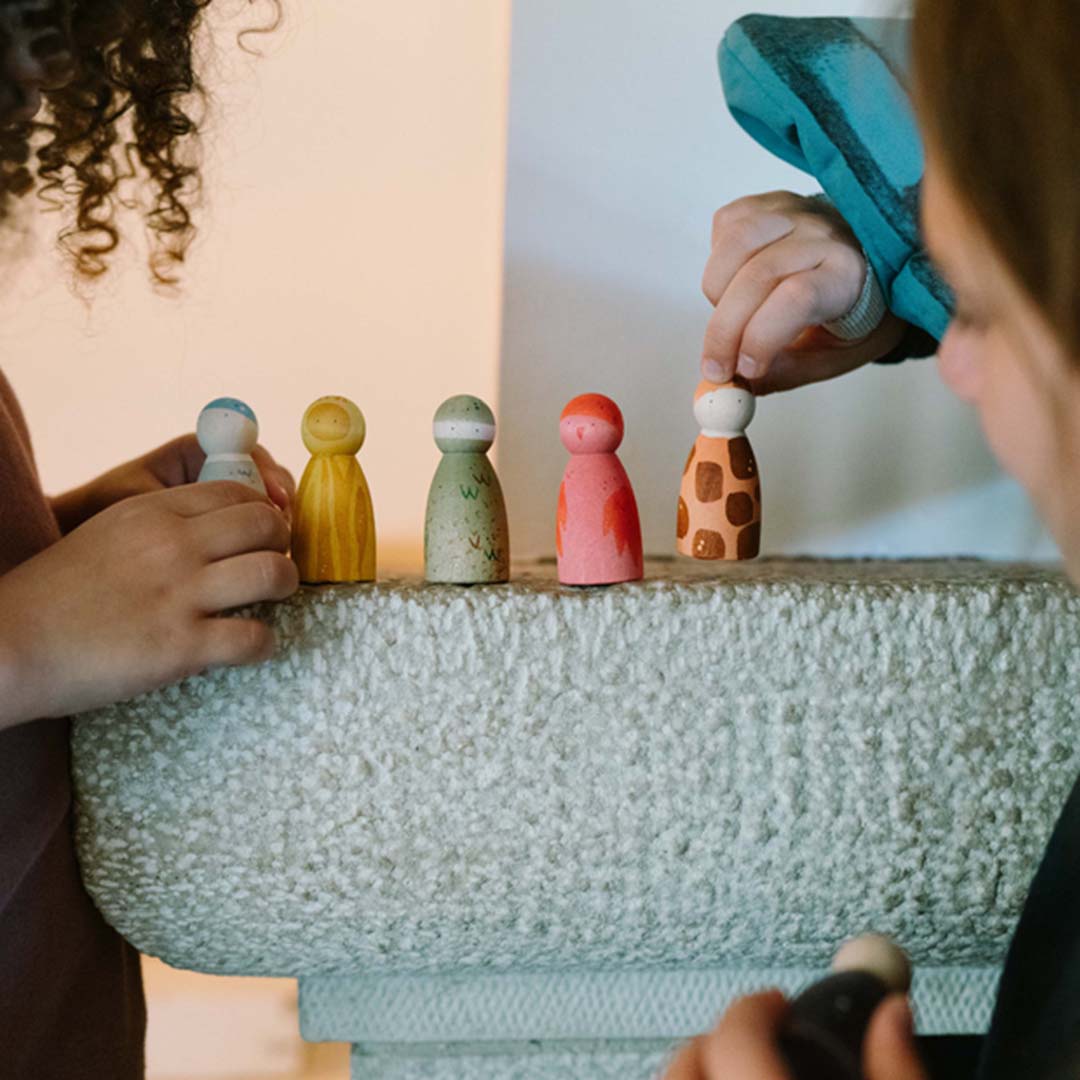 Twee kinderen spelen met vijf Grapat houten dierenfiguurtjes op een stenen ondergrond.