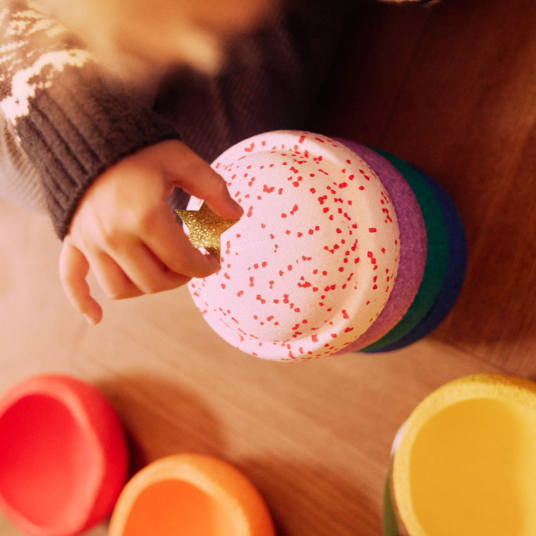Een kinderhand pakt een gouden ster uit een roze stapelstein babyspeelgoed schijf met rode stippen.