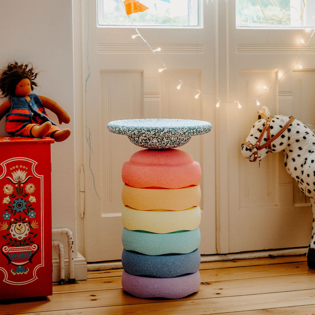 Gestapelde stapelstein bouwstenen in pastel regenboogkleuren in een speelkamer met een pop en speelgoedpaard.
