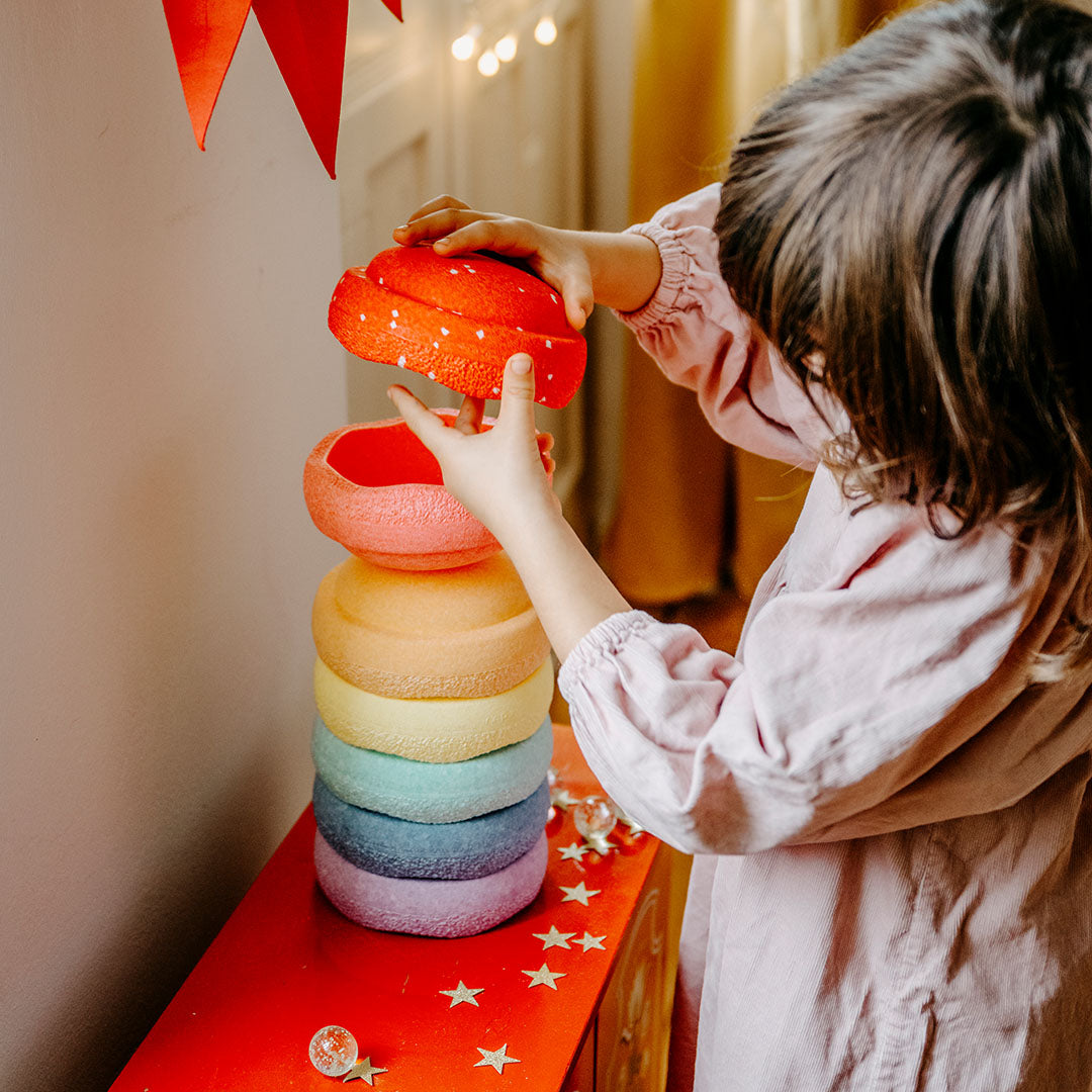 Een kind plaatst de rode stapelstein steen met stippen op een toren van pastelkleurige stapelstenen.