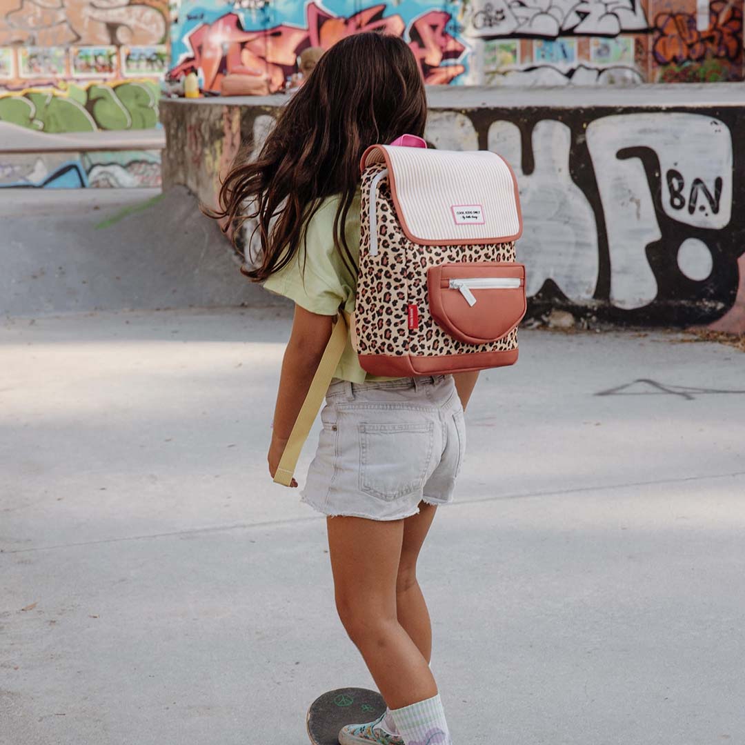 Kind met een Hello Hossy schoolrugzak met luipaardprint staat op een skateboard in een skatepark.