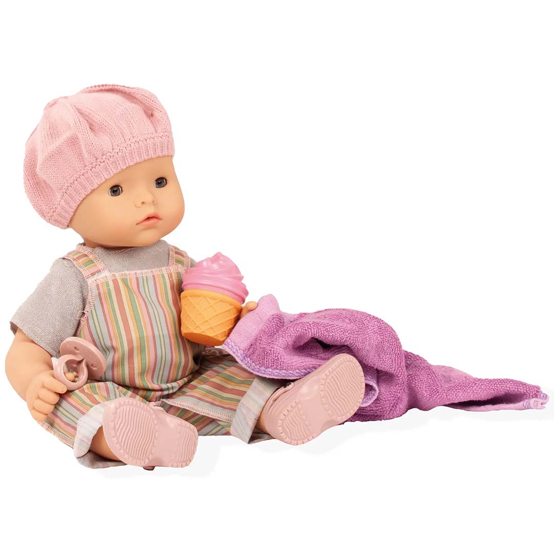 Götz waterdichte babypop met roze muts, gestreepte salopette, ijsje, speen en paarse handdoek.