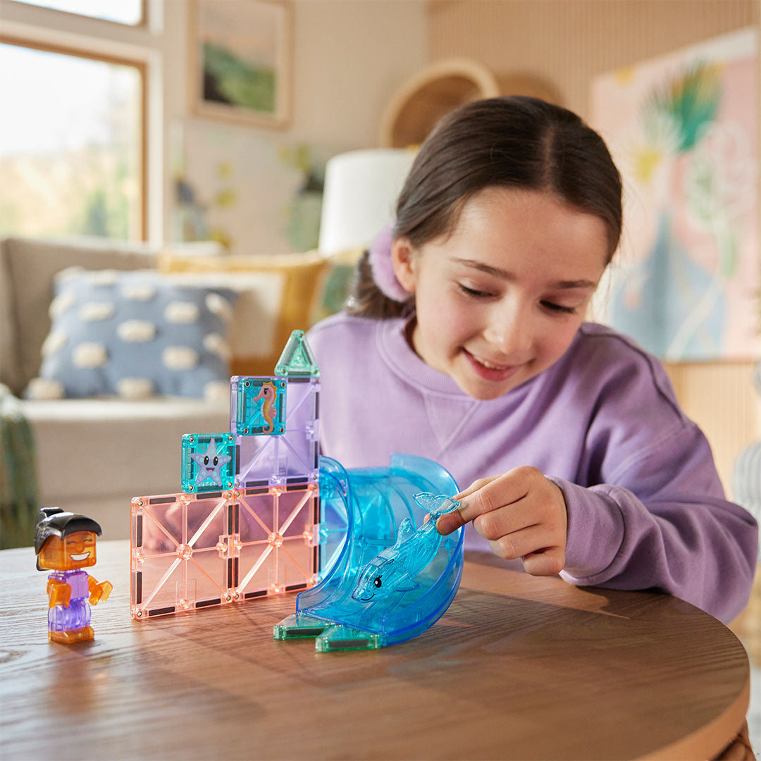 Een meisje speelt met de Magna-Tiles Dolphin Bay magnetische tegels bouwset met een dolfijn en een glijbaan.