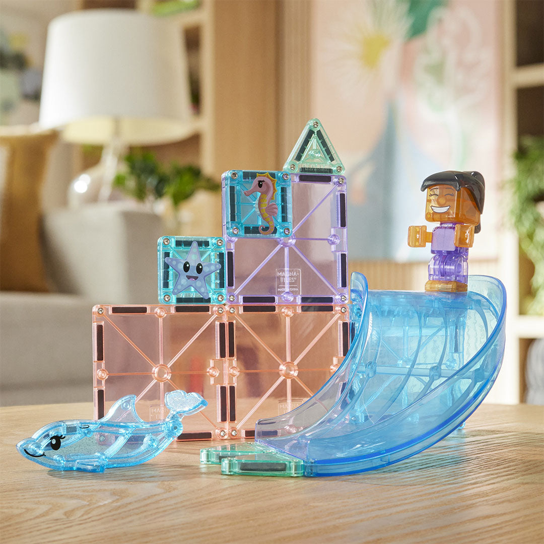 De Magna-Tiles Dolphin Bay magnetische tegels bouwset met een dolfijn, een glijbaan en een figuurtje op een houten tafel.
