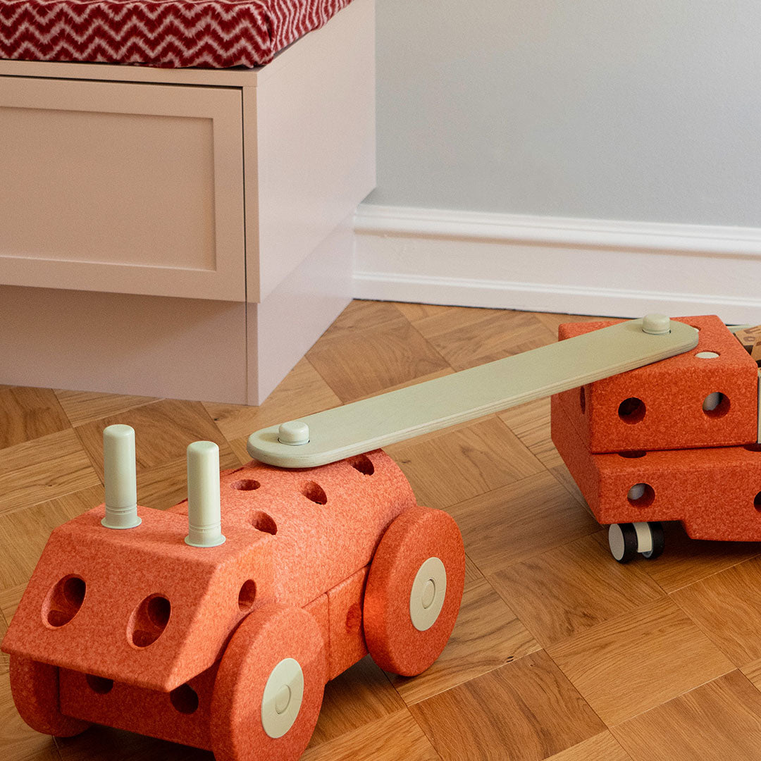 Een speelgoedvoertuig gemaakt van modu bouwblokken en een evenwichtsbalk, staand op een houten vloer.