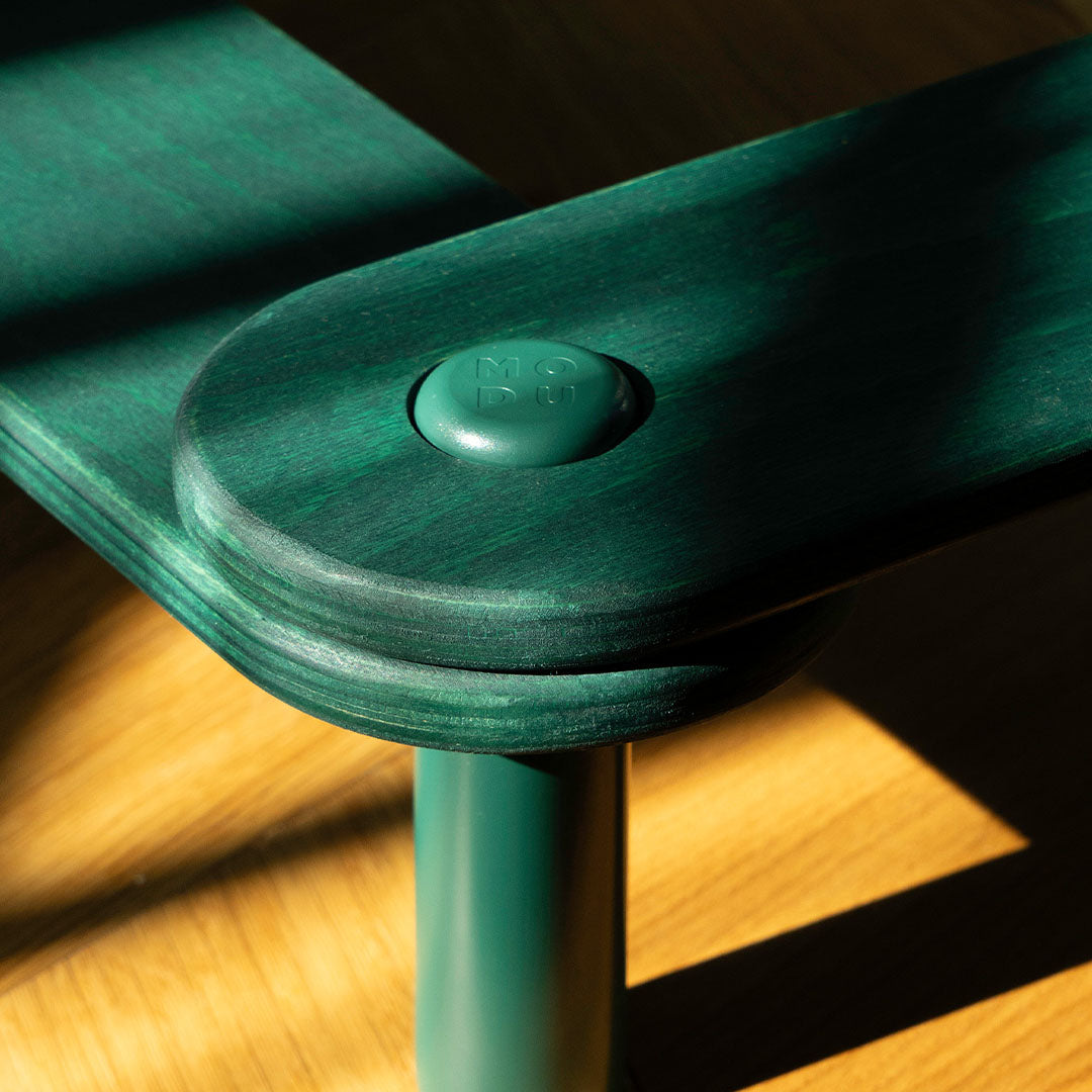 Close-up van een groene houten modu evenwichtsbalk met een verbindingsstuk en het modu logo.