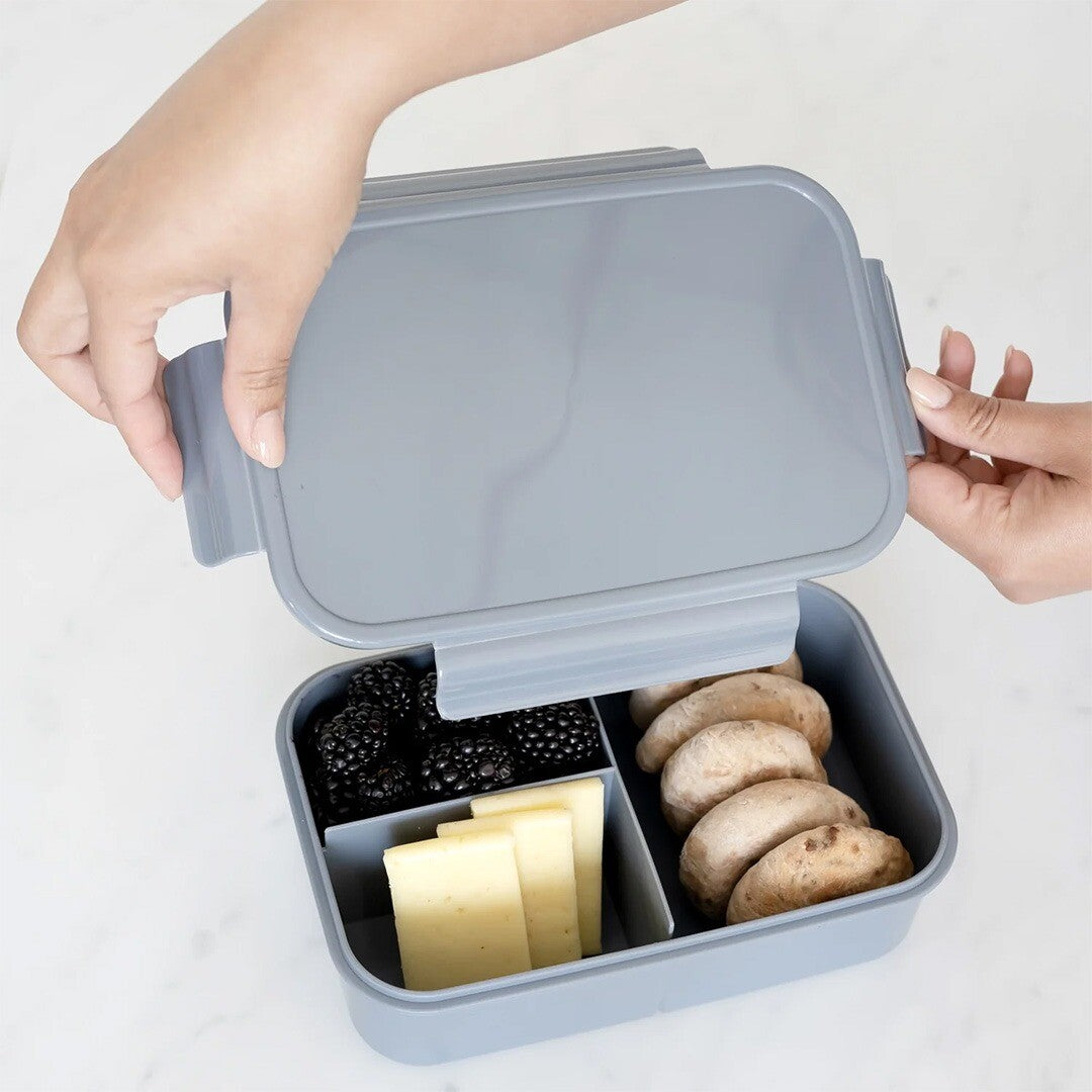 Handen openen de 3 sprouts bento kinder lunchbox gevuld met fruit, kaas en broodjes.