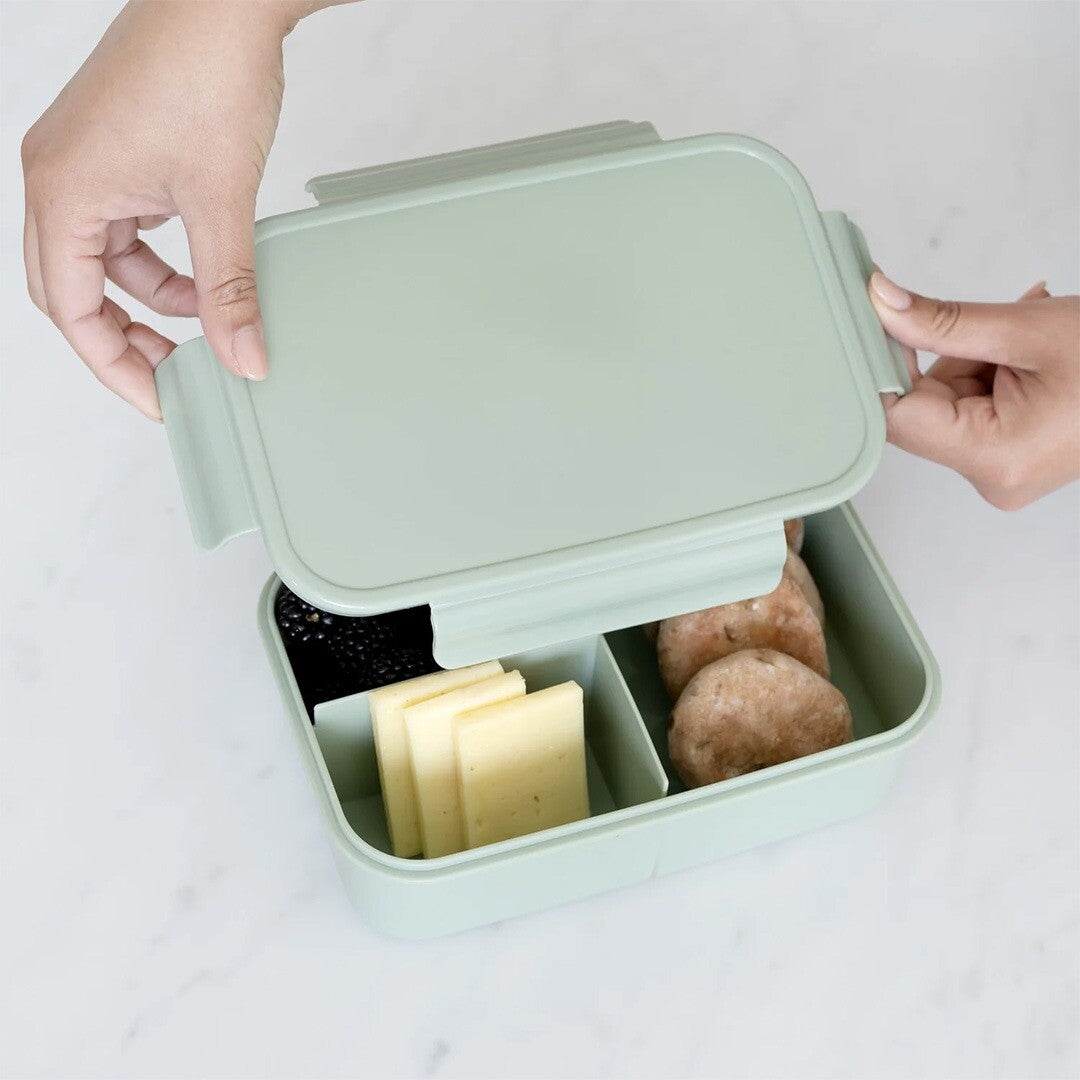 Twee handen plaatsen de deksel op de 3 sprouts groene bento broodtrommel gevuld met eten.