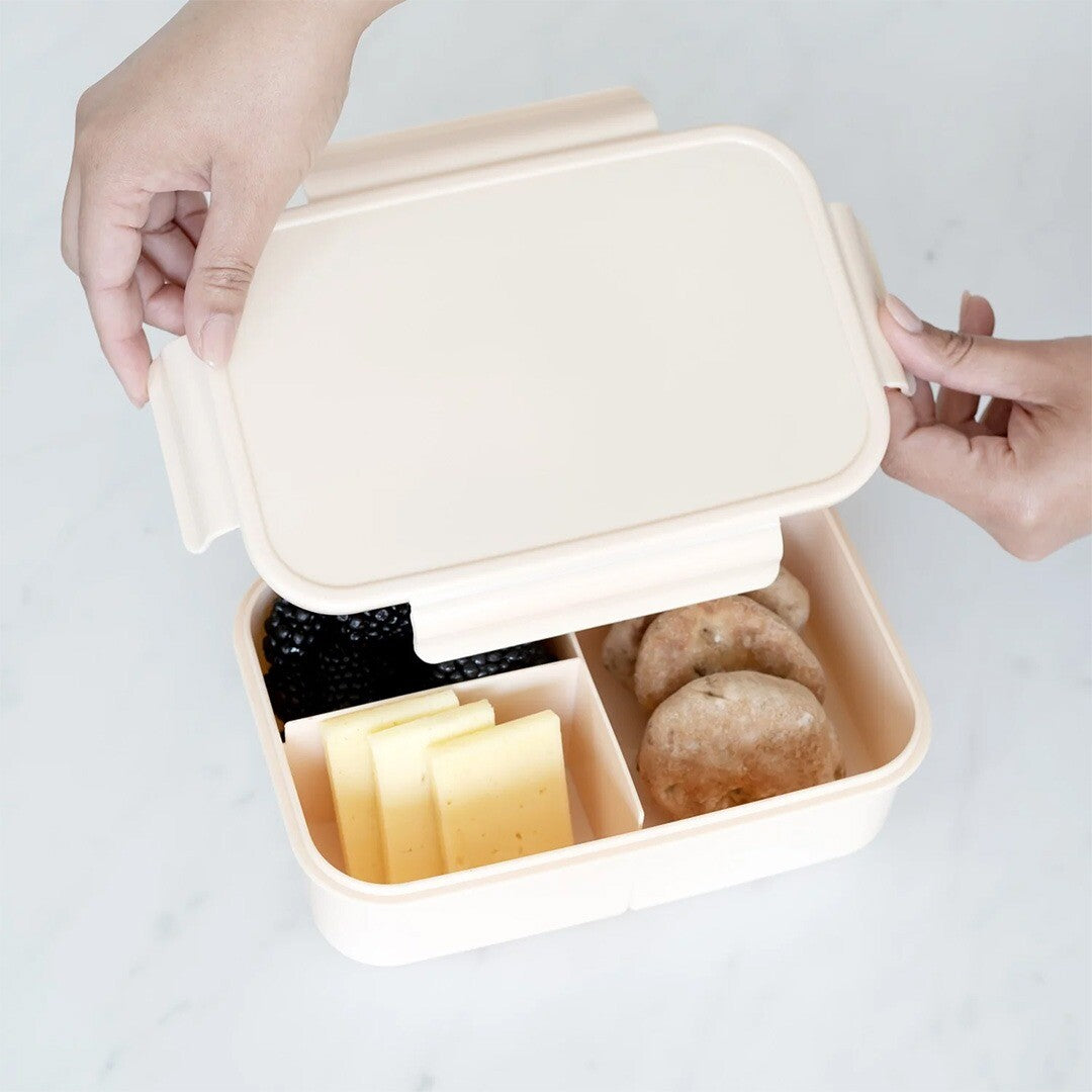 Handen openen de 3 sprouts bento broodtrommel gevuld met fruit, kaas en koekjes.