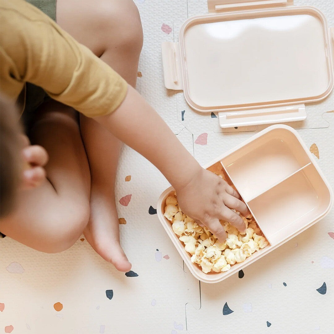 Een kind pakt popcorn uit de open 3 sprouts bento broodtrommel met meerdere vakken.