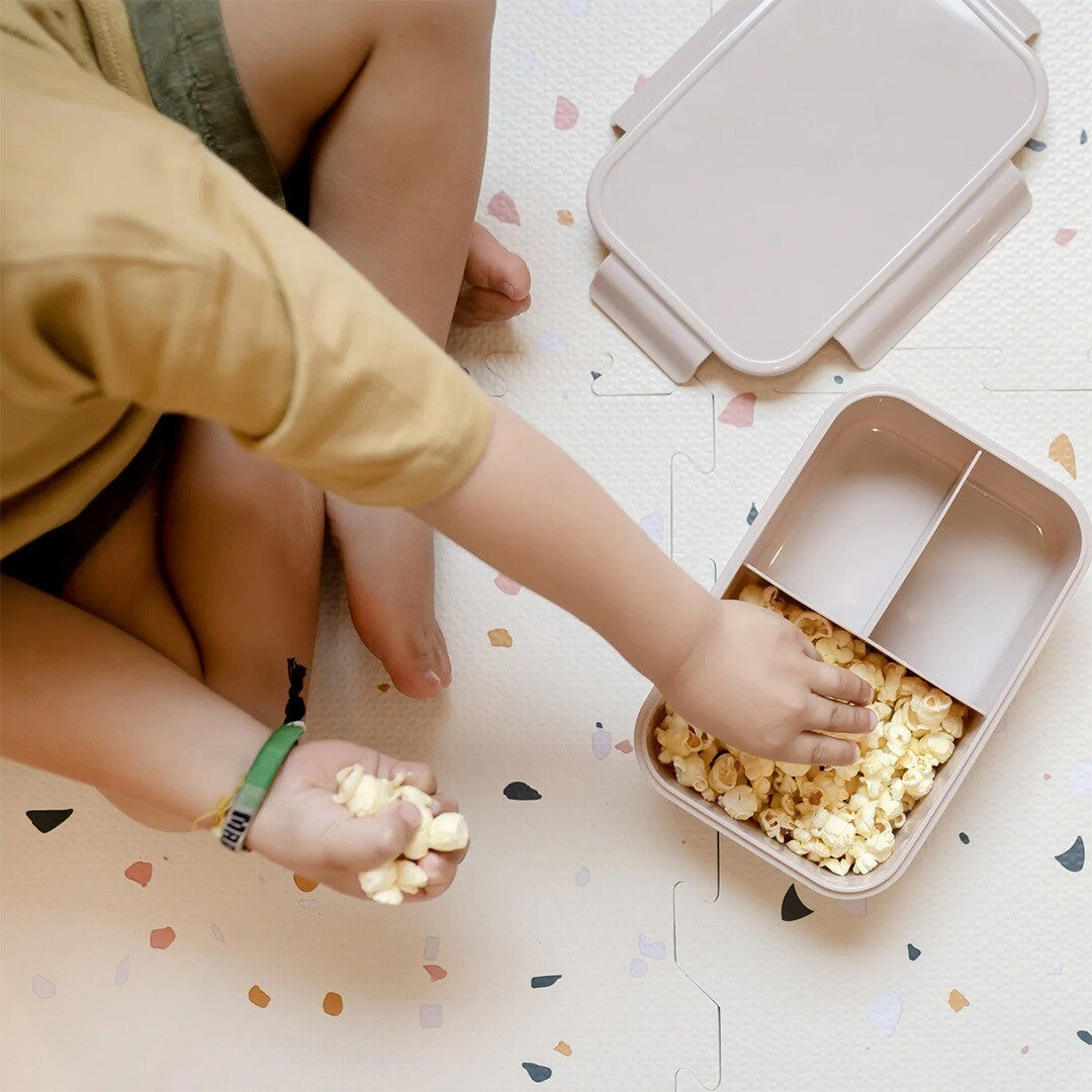 Een kind pakt popcorn uit de open 3 sprouts bento broodtrommel.