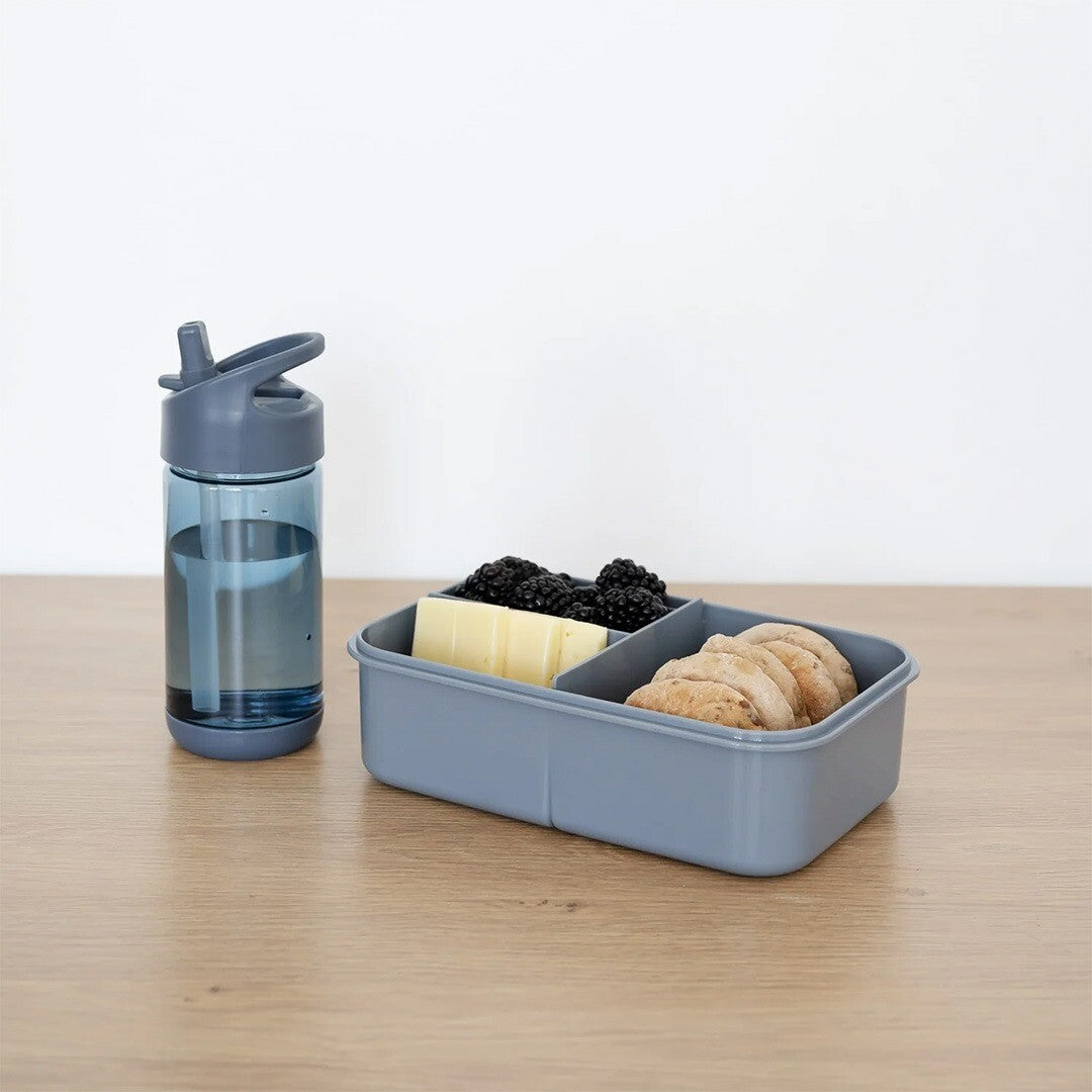 De blauwe 3 sprouts drinkfles staat naast een grijze lunchbox met fruit en koekjes.
