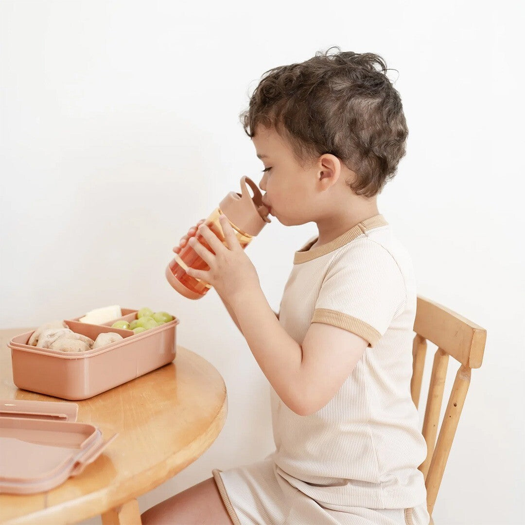 Een kind drinkt uit de 3 sprouts kinder drinkfles aan tafel, naast een lunchbox.