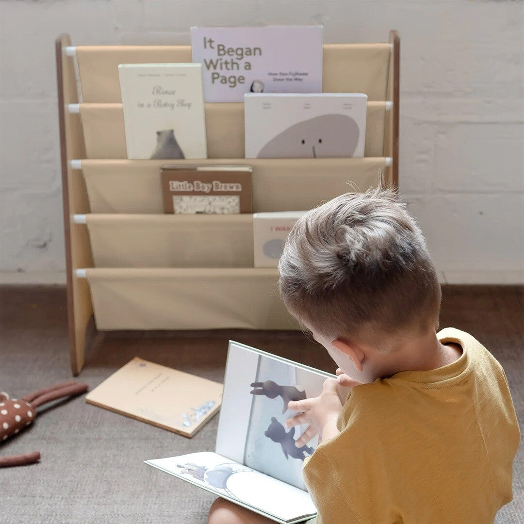 Een kind leest een boek voor een 3 sprouts kinderboekenrek gevuld met boeken.